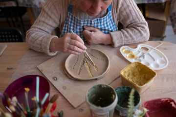 Senior female artist making flower ornament on ceramic product.