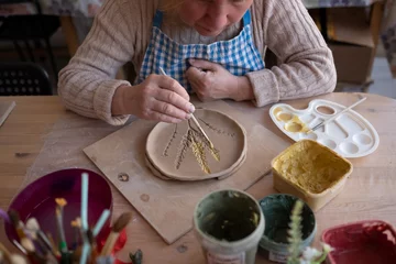 Foto op Canvas Senior female artist making flower ornament on ceramic product. © Viktor Koldunov