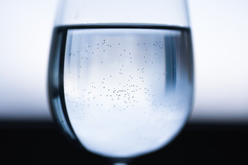 Transparent wine glass with water in the middle, small bubbles. Blue black white blurred...