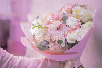 A hand is holding a lush bouquet of light pink, white cute delicate small roses of different sizes, flowers of green leaves. Paper packaging. Romance.