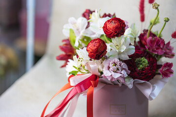 Red and white different flowers in a round pink box vase with shiny ribbons. Gift concept. Studio