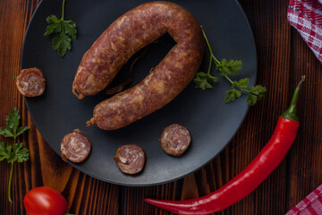 Smoked sausage ring with spices and herbs. Traditional Ukrainian snacks, cutting board, cold smoked meat cutting on a black plate. Top view. Free space for text.
