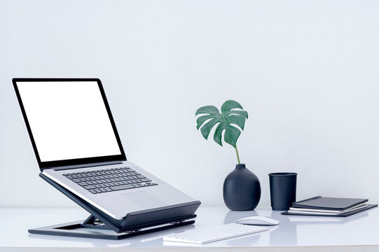 Mockup blank screen laptop computer on wooden stand with keyboard and mouse on white top table.
