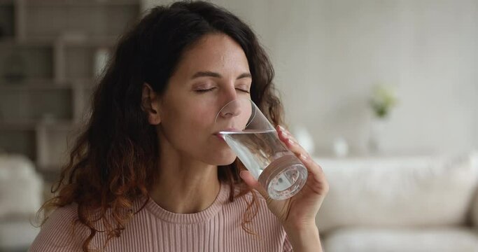 Close up view beautiful thirsty young woman sit alone indoor holding glass of natural aqua make sips drinks still water preventing dehydration. Good life habits, healthy slimming, weight loss concept