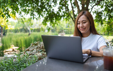 A young asian woman working and typing on laptop keyboard while sitting in the park