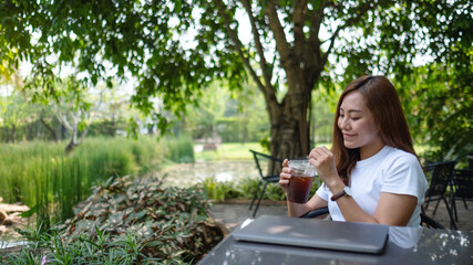 A young asian woman drinking coffee after finish working on laptop on the table in the outdoors