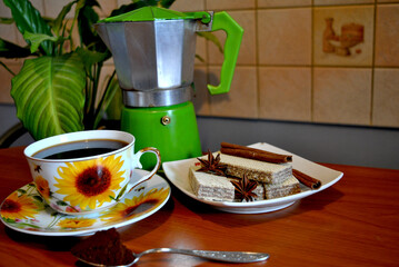 Zdjęcie przedstawiające filiżankę kawy z wafelkami na stole z kawiarką w tle - obrazy, fototapety, plakaty