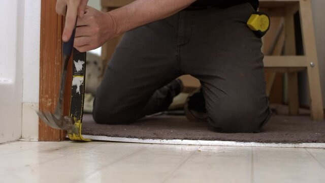 Man using a hammer and prybar to remove a carpet and runner in a bathroom during a remodel