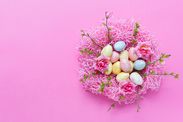 Easter composition with spring foliage branches and pink nest filled with small colorful eggs on pink background
