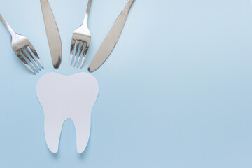 One large paper tooth with eating utencils forks and knifes on blue background