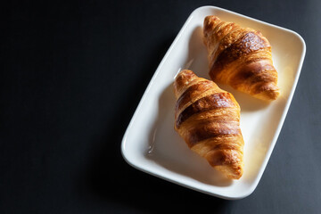 French croissant on white plate on black table background and nature sunlight with shadow through from window.