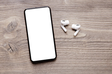Phone with empty blank screen with wireless earphones on wooden background