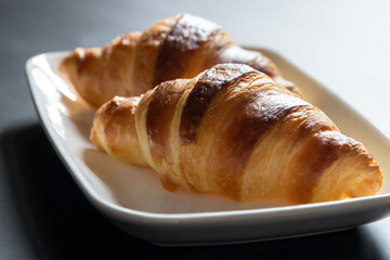 French croissant on white plate on black table background and nature sunlight with shadow through from window.