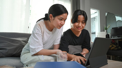 Two young asian girl using computer tablet while sitting together on sofa in living room.