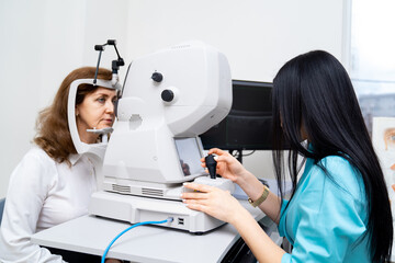Brunette female opthometrist is diagnosing senior woman on special modern equipment. Up-to-date clinic for healthy eyes. Closeup.
