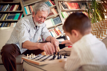 Grandpa and his little grandson playing the chess at home. Family, game, together