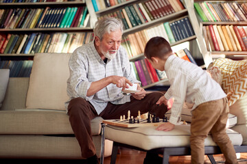 Grandpa and his little grandson having fun while playing the chess game at home. Family, game, together