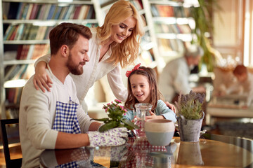 Cheerful parents spend quality time with their little daughter while planting the plant at home together. Family, leisure, together