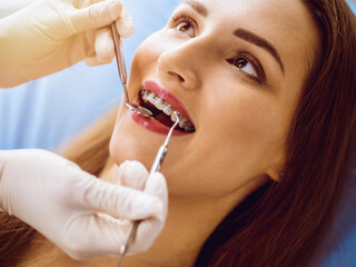 Smiling young woman with orthodontic brackets examined by dentist in sunny dental clinic. Healthy...
