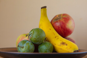 Homemade still life of a plate of seasonal fruits, a delicious vegetarian dessert of banana, apple and plums. Raw, healthy and unprocessed food, tasty, sweet and juicy fruits. Spain.