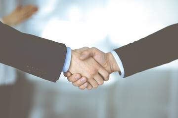 Business people shaking hands at meeting or negotiation, close-up. Group of unknown businessmen and a woman standing in a modern office. Teamwork, partnership and handshake concept