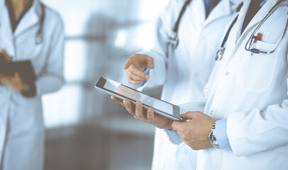 Group of unknown doctors use a computer tablet to check up some medical names records, while...
