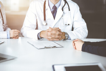 Fototapeta premium Unknown male doctor listening to his patient woman while sitting in sunny clinic. Medicine concept during Coronavirus pandemic. Covid 2019