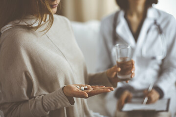 Close-up woman-patient holding pills near her doctor, time to take medications, cure for headache or remedy pain killer drugs. Stay at home concept during Coronavirus pandemic and self isolation