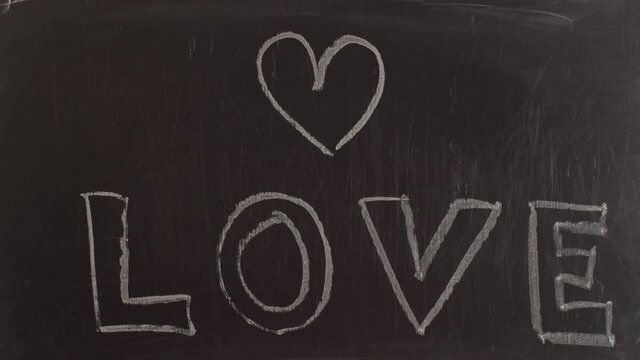 Word love written by hand in voluminous letters on chalkboard. Heart is painted with chalk on blackboard and word love written.