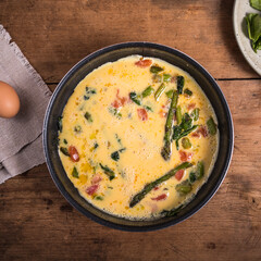 Cooking omelette with asparagus, tomatoes and spinach - mixed eggs poured into the pan with asparagus, tomatoes and spinach.