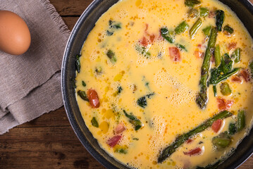 Cooking omelette with asparagus, tomatoes and spinach - mixed eggs poured into the pan with asparagus, tomatoes and spinach.