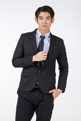 Portrait shot of Asian young black short hair smart confident businessman entrepreneur in formal suit with necktie standing smiling keep hand in pockets look at camera in front of white background