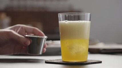 Slow motion man pour aperitivo in orange soda with ice in tumbler glass to make spritz drink on concrete countertop - Powered by Adobe