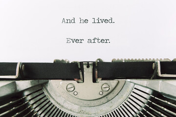 The ending phrase And he lived, ever after (intentionally missing the word happily), printed on a paper page inside an old vintage typewriter. Closeup shot.
