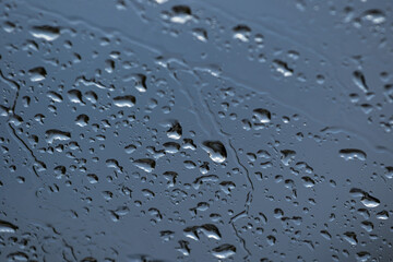 The background and texture of raindrops on the beveled windshield of the car against the dark blue cloudy sky with blur on parts of the frame in bad weather. High quality photo