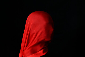 Mannequin head with large red silk scarf covering the face, black background.