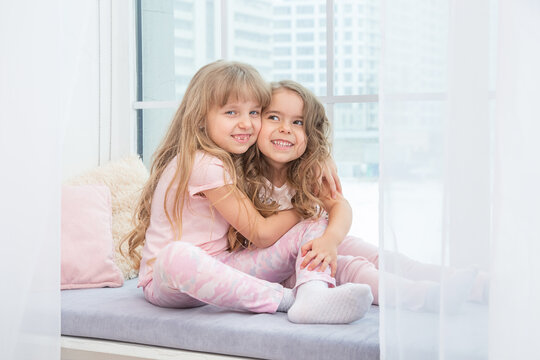 Cute little siblings sitting on windowsill at home hugging