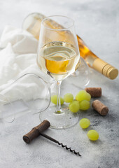 Glass of white refreshing wine with grapes and corkscrew and bottle on light background.