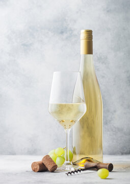Glass and bottle of white wine with grapes and corkscrew on light background.