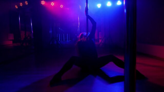 Woman dances a sensual sexy dance on the floor near pole in the dark. Pole dance