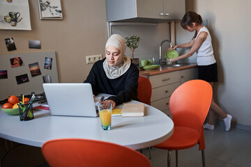 Woman wearing hijab making some notes while doing her home task