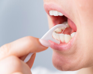 Caucasian woman brushing teeth with toothpick with dental floss on white background.