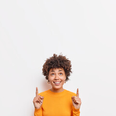 Photo of cheerful African American female points fingers up at top promo text suggests to check out awesome offer demonstrates copy space banner against white background wears casual jumper. - obrazy, fototapety, plakaty
