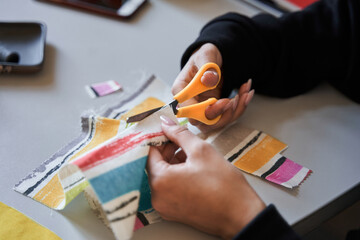 Woman holding scissors and cutting a piece of the colorful fabric while sewing