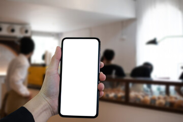 Hand holding white mobile phone with blank white screen in cafe.