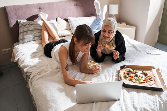 Girls Of Different Religion Laying At The Bedroom And Eating Tasty Pizza Calmly