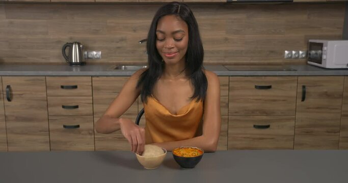 Young African woman sitting in kitchen and eating Egusi soup with eba using fingers. West African traditional dishes.