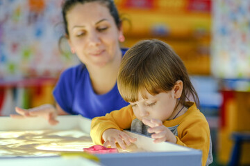 Fototapeta premium Creative early baby development. A mother teaches her child to draw with her fingers in the sand. Center for the Development of Children with Autism.