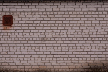 A white brick wall, blackened with age. Ventilation window.