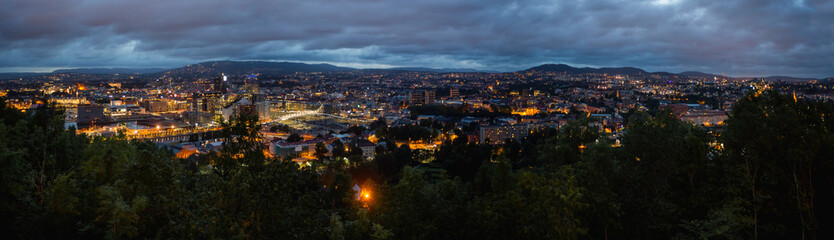 Fototapeta premium Night panoramic view of Oslo, capital of Norway. Dark cloudscape ower capital of Norway. Scandinavian city with lighted buildings and bridges, surrounded by forests.